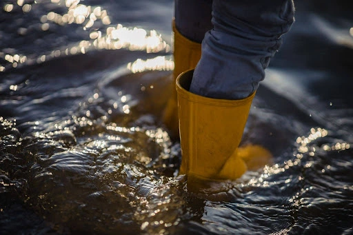 Yellow rainboots wading through deep floodwater.