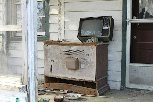 Old water-damaged TV and wooden console on a ruined porch.